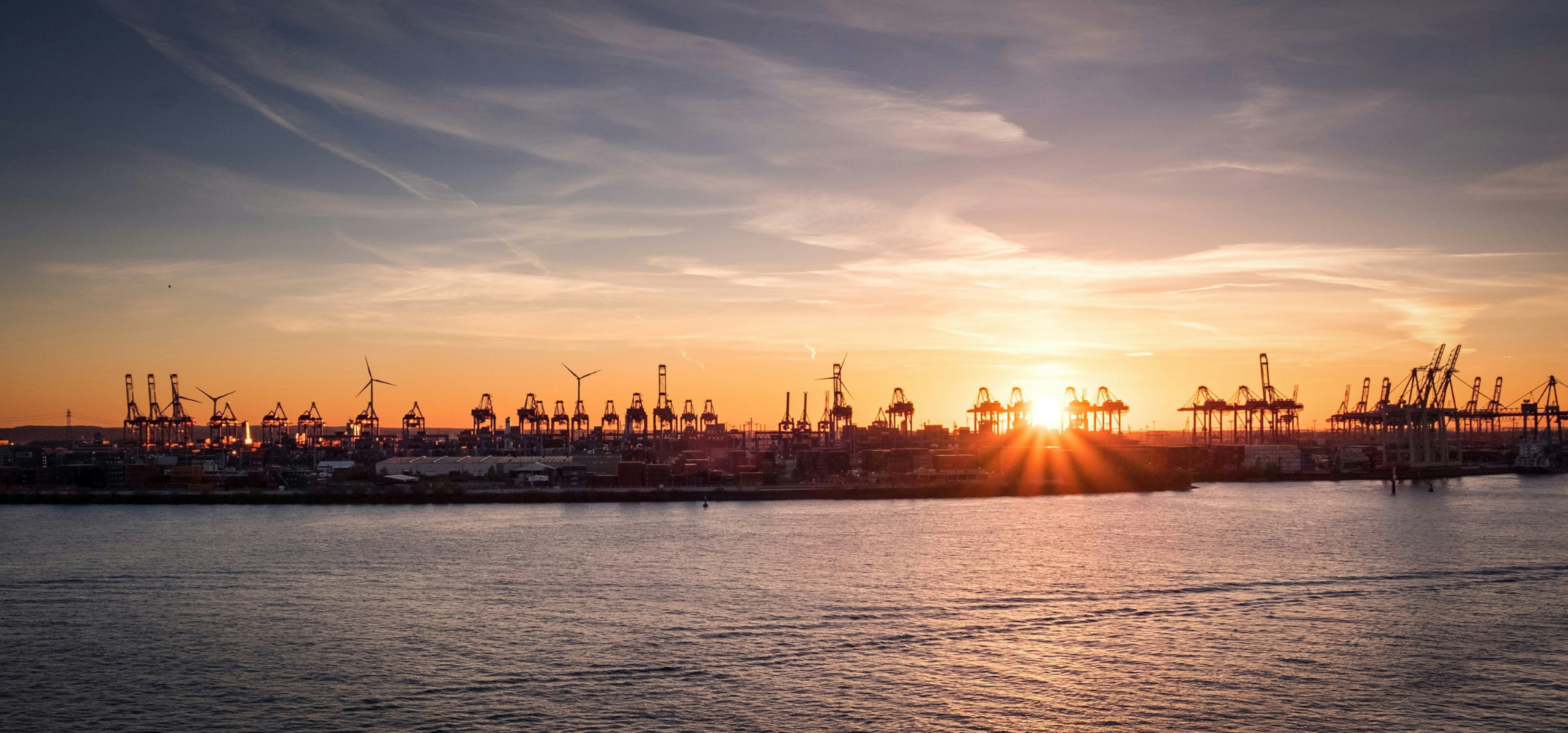 sun rising over a shipping port